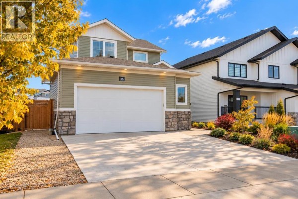 Front exterior of a two-story green house with a double garage and landscaped front yard. - 85 Crestview Boulevard, Sylvan Lake