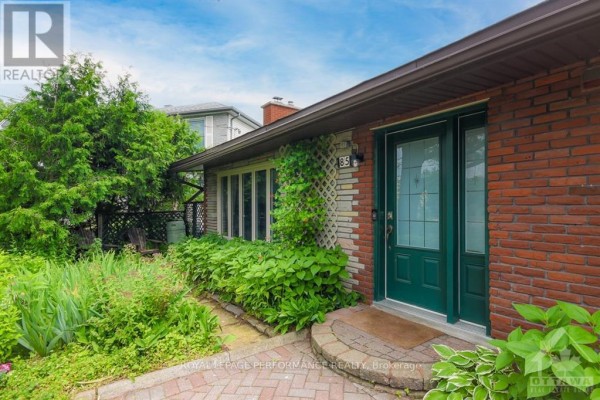 Close-up of the front entrance with a green door, brick facade, and surrounding plants. - 85 Crownhill Street, Ottawa