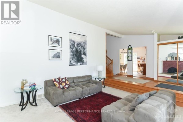 Living room with a brick fireplace, large window, plush seating, and hardwood floors. - 85 Crownhill Street, Ottawa