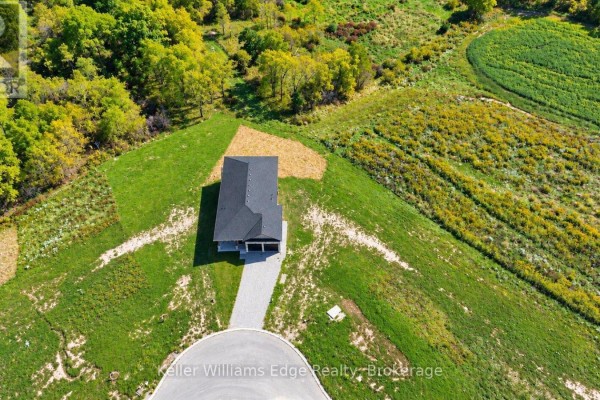 Overhead view of a modern house with a grey facade, dark roof, and paved driveway on a grassy slope. - 85 Pike Creek Drive, Haldimand