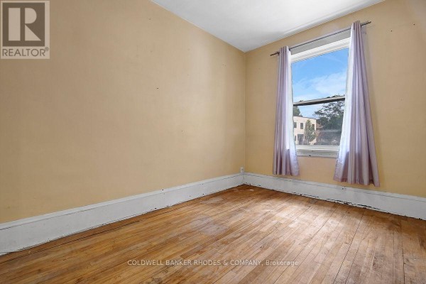 Empty room with hardwood floors, cream walls, and a large window with curtains. - 85 Richmond Road, Ottawa