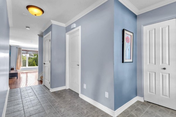 Interior hallway with light blue walls, grey tiled floor, white doors, and a view of a living area with wood floors. - 85 Rue De La Pointe-taillon, Gatineau