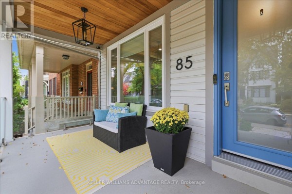 A covered porch with seating, yellow rug, potted plant, and blue front door. - 85 Sarah Ashbridge Avenue, Toronto
