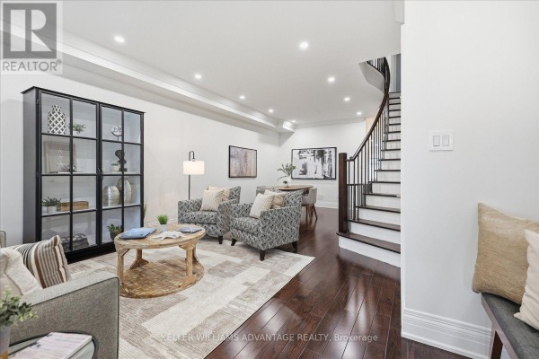 A living room with dark hardwood floors, a glass display cabinet, and two patterned armchairs. - 85 Sarah Ashbridge Avenue, Toronto