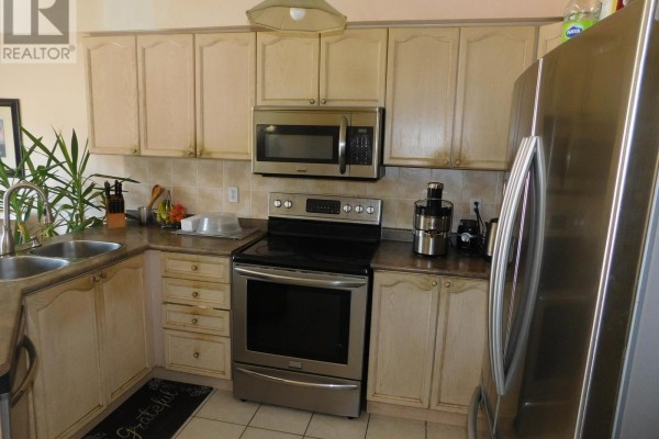 A kitchen with light wood cabinets, stainless steel appliances, and a double sink. - 85 Weather Vane Lane E, Brampton