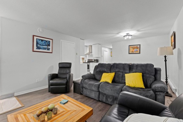 Living room with dark gray reclining sofa, armchair, and view into the kitchen area. - 850 Boul. St-rené O., #2, Gatineau