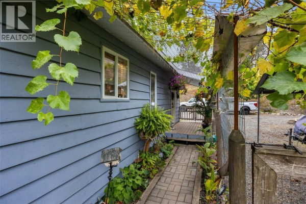 Pathway leading to a covered porch with blue siding and greenery. - 850 Inskip Road, Kamloops
