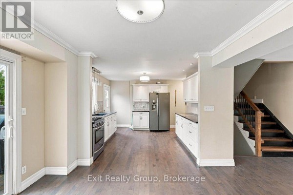 Open-concept kitchen and living area with dark wood floors, white cabinets, and a staircase. - 850 Littlestone Crescent, Kingston