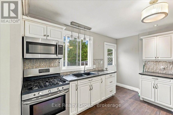 Kitchen area with stainless steel appliances, white cabinets, dark countertops, and a double sink. - 850 Littlestone Crescent, Kingston