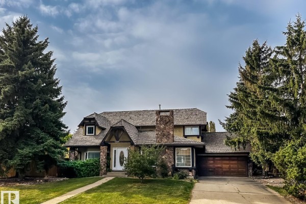 Front view of a large house with a stone chimney and mature trees. - 8504 173 St Nw, Edmonton