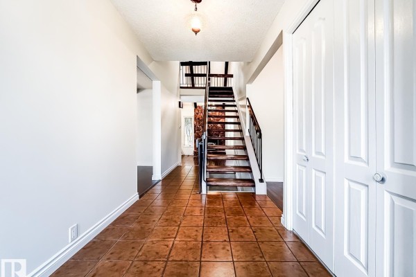 Entrance hallway with tan tile flooring, white walls, and dark wood staircase. - 8504 173 St Nw, Edmonton