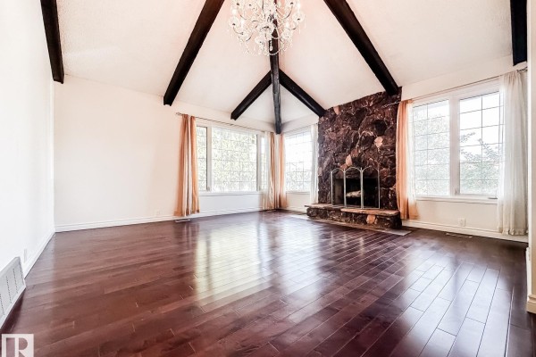 Living room with vaulted ceiling, dark wood beams, stone fireplace, and hardwood floors. - 8504 173 St Nw, Edmonton