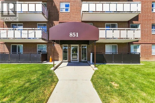 Entrance to apartment building 851 with a dark brown awning over glass doors. - 851 Queenston Road Unit# 202, Hamilton