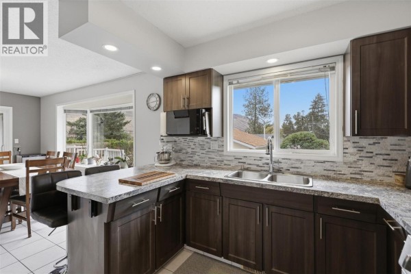 Kitchen with dark wood cabinets, granite countertops, stainless steel sink, and view of the backyard. - 851 Sumac Place, Kamloops