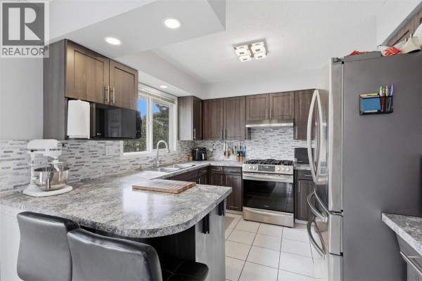 Kitchen with dark wood cabinets, granite countertops, stainless steel appliances, and tiled flooring. - 851 Sumac Place, Kamloops