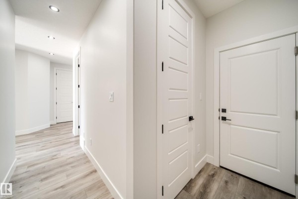 Hallway with white walls, several doors, and light wood laminate flooring. - 8515 183 Av Nw, Edmonton