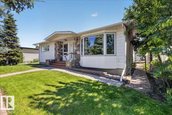 Front corner view of a white bungalow with stone accents and a paved side path. - 8515 56 St Nw, Edmonton