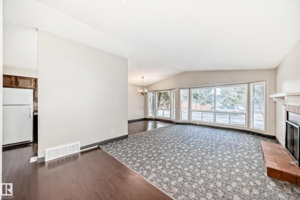 Living room featuring bay windows, chandelier, and a brick fireplace. - 8516 190 St Nw, Edmonton