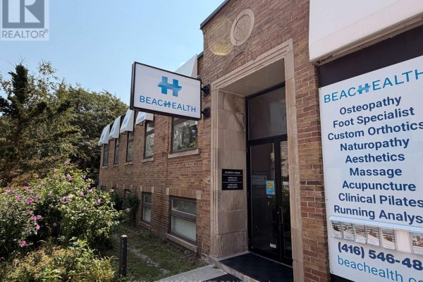 Close-up of the brick building entrance with a Beach Health sign and a list of available services. - 2, 3, 4 - 855 Kingston Road, Toronto