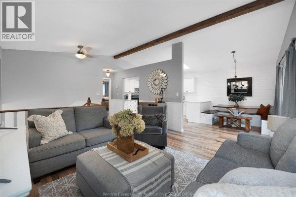 Living room with grey sofas, ottoman, wood beam ceiling, and view into the kitchen area. - 856 Lawndale Avenue, Kingsville