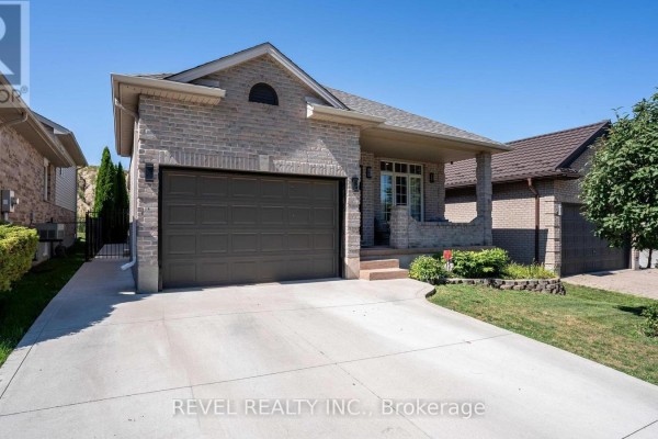Side exterior view of a brick house with a grey garage door and concrete driveway. - 857 Cresthaven Crescent, London South