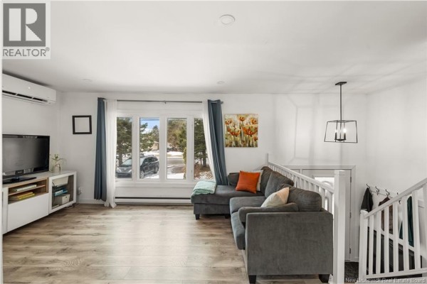 Cozy living area with a TV, bookshelf, and large windows for natural light. - 857 Mapleton Road, Moncton