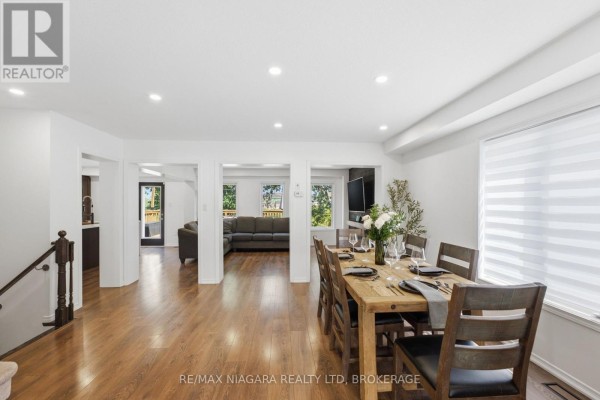 Dining room with a wooden table set for six, view into a living room, and hardwood floors. - 8571 Dogwood Crescent, Niagara Falls
