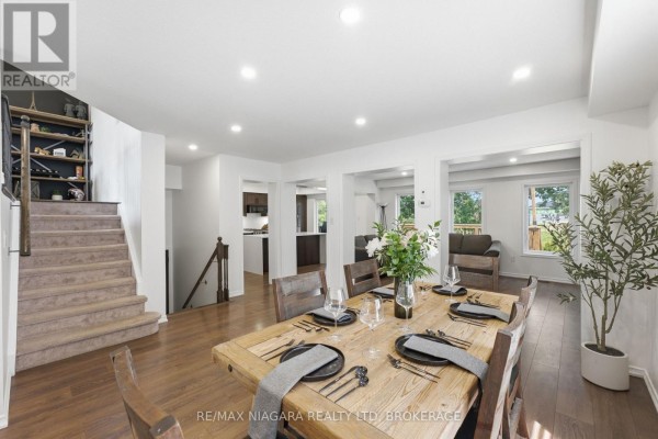 Dining area with a large wooden table, view of the living room and kitchen, and carpeted stairs. - 8571 Dogwood Crescent, Niagara Falls