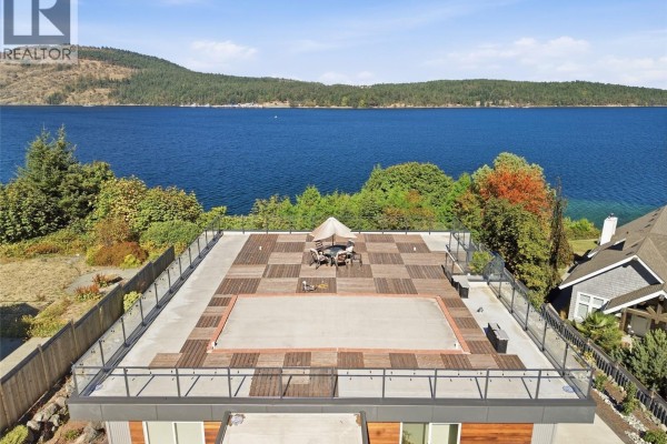 Aerial view of the flat roof deck with wood decking, glass railings, and a covered seating area. - 8578 Rumming Rd, Lantzville