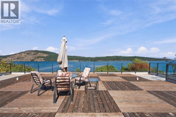 Close-up of a wooden deck with outdoor chairs and a table on a sunny day with ocean view. - 8578 Rumming Rd, Lantzville