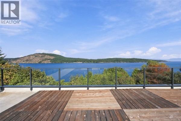 View from the rooftop deck showing wooden planks, glass railings, and a calm blue ocean. - 8578 Rumming Rd, Lantzville