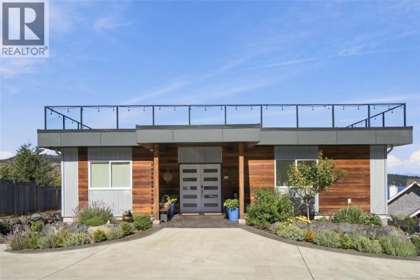 Front view of a modern home with a long driveway, wood and metal siding, and a flat roof deck. - 8578 Rumming Rd, Lantzville