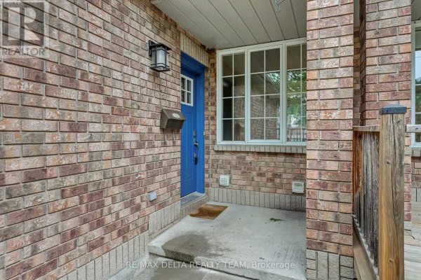 Close-up of the townhouse entrance with a blue door, brick facade, and porch light. - 858 Como Crescent, Ottawa