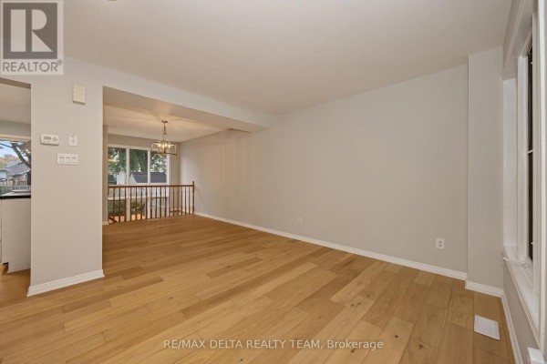 Living room with light oak hardwood floors, light grey walls, and a view of the dining area. - 858 Como Crescent, Ottawa