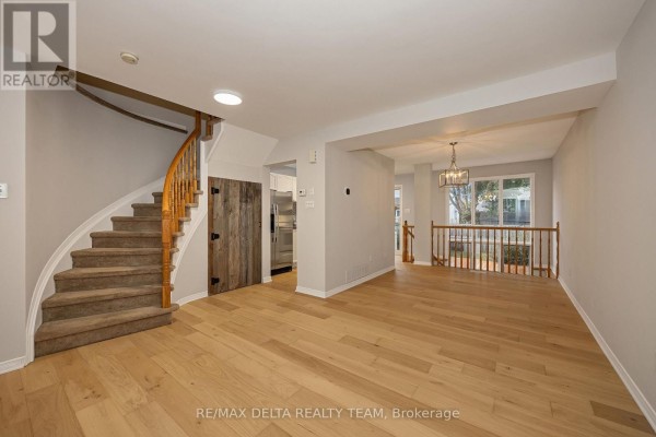 Open-concept living and dining area with light oak floors, grey walls, and a curved staircase. - 858 Como Crescent, Ottawa