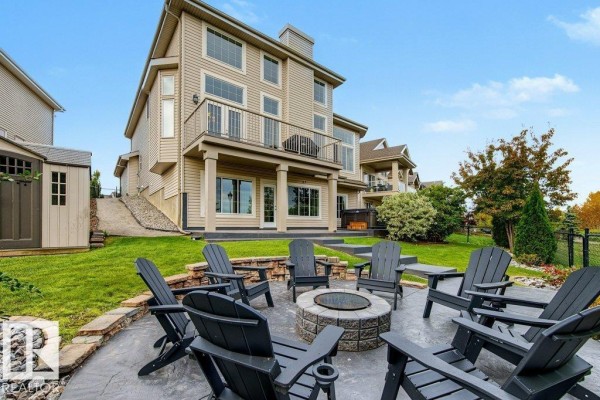 Backyard patio with a fire pit, Adirondack chairs, and a multi-level house with a deck. - 858 Hodgins Rd Nw Nw, Edmonton