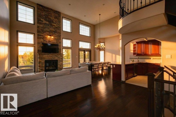 Living room with a stone fireplace, large windows, a sectional sofa, and a view of the dining room and kitchen. - 858 Hodgins Rd Nw Nw, Edmonton