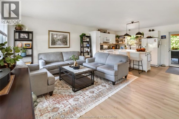Living room with grey sofas and armchairs around a coffee table, open to kitchen. - 8585 James Street, Charing Cross
