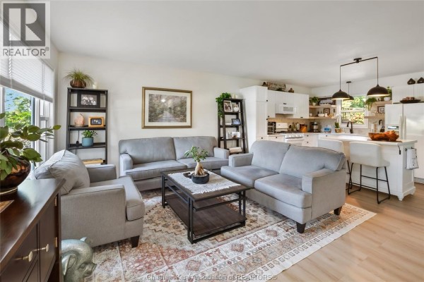 Living area with grey seating and a view into the white kitchen with island. - 8585 James Street, Charing Cross