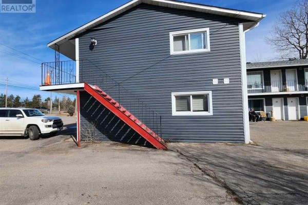 Side view of a commercial building showing an exterior staircase and parked vehicles. - 859 Trunk Rd, Sault Ste  Marie