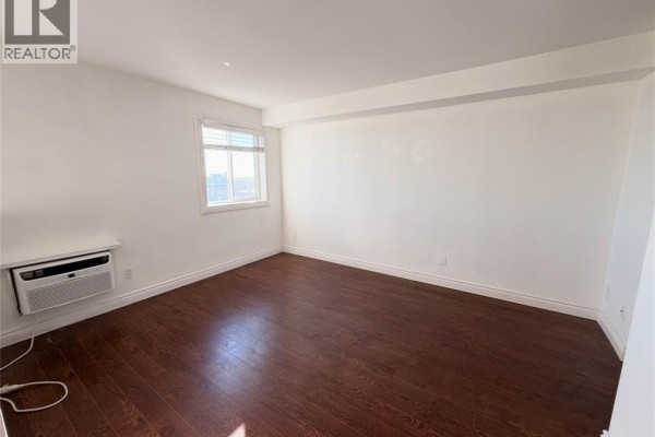 Empty bedroom with dark wood floors, white walls, and a window with blinds. - 8591 Riverside Drive East Unit# 1303, Windsor