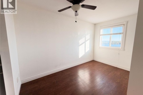 Bedroom with dark wood floors, white walls, a ceiling fan, and a window with a water view. - 8591 Riverside Drive East Unit# 1303, Windsor