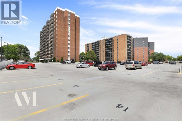 Parking lot with multiple vehicles and apartment buildings in the background. - 8591 Riverside Drive East Unit# 308, Windsor