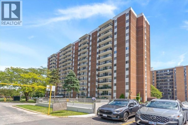 Side exterior view of a brick apartment building with parked cars in the foreground. - 8591 Riverside Drive East Unit# 702, Windsor