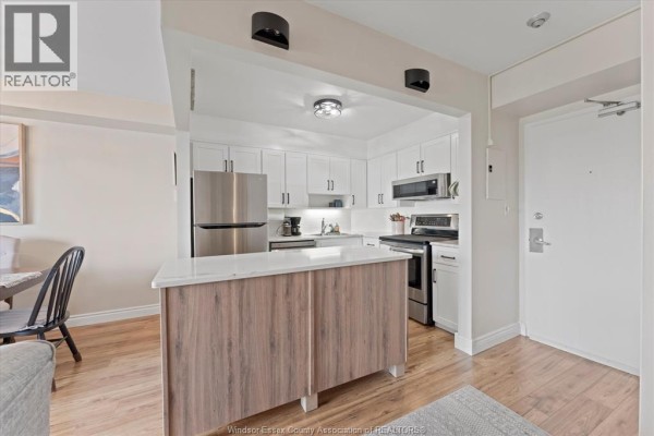 Modern kitchen with white cabinets, stainless steel appliances, and a wood-accent island. - 8591 Riverside Drive East Unit# 702, Windsor
