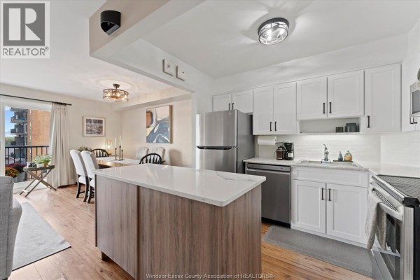 Open concept living and dining area adjacent to a modern kitchen with white cabinets. - 8591 Riverside Drive East Unit# 702, Windsor
