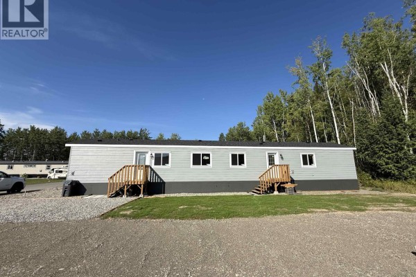 Wide view of the light grey mobile home exterior showing the full length and the surrounding gravel and grass. - 86 313 Westland Road, Quesnel