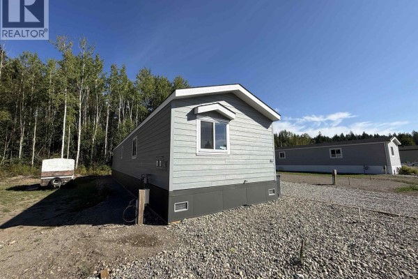 Side exterior of the light grey mobile home showing a window and skirting around the base. - 86 313 Westland Road, Quesnel