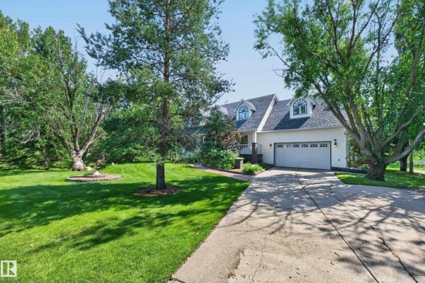 White house with attached double garage, grey roof, and mature trees in the yard. - #86 52514 Rge Road 223, Rural Strathcona County