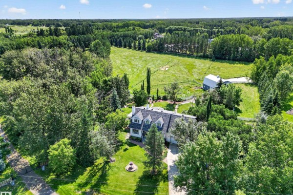 Aerial view of a white house with grey roof and garage, situated on a large property with a field and barn. - #86 52514 Rge Road 223, Rural Strathcona County